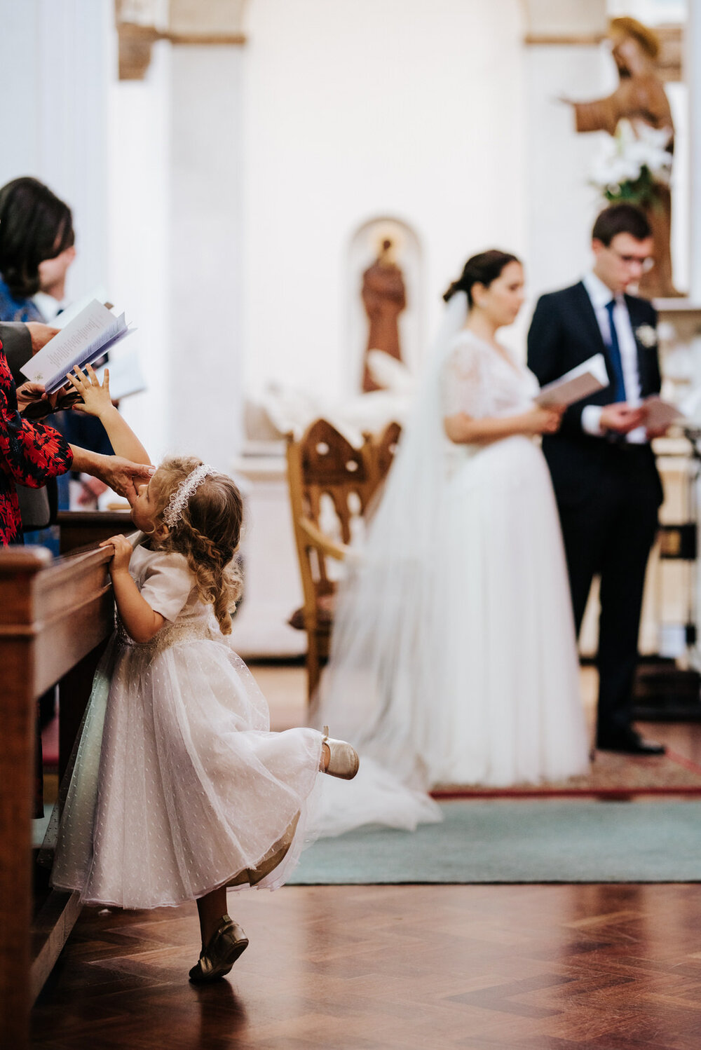 Little girl plays and twirls in church as bride and groom sing hymns in the background