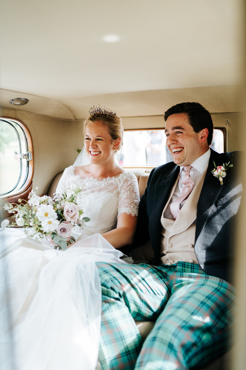 Bride and groom sit inside car right after wedding ceremony and smile with excitement