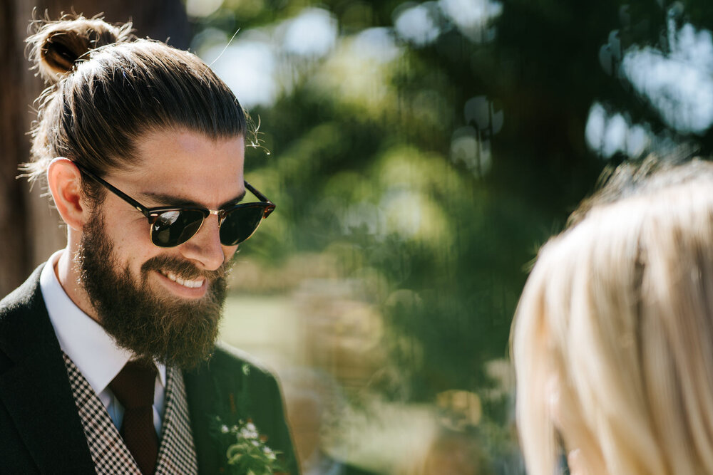 Fashionable groom smiles at bride during wedding ceremony