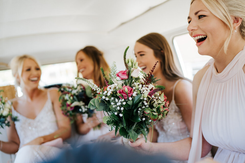 Bridesmaids smile and cheer inside campervan on their way to ceremony