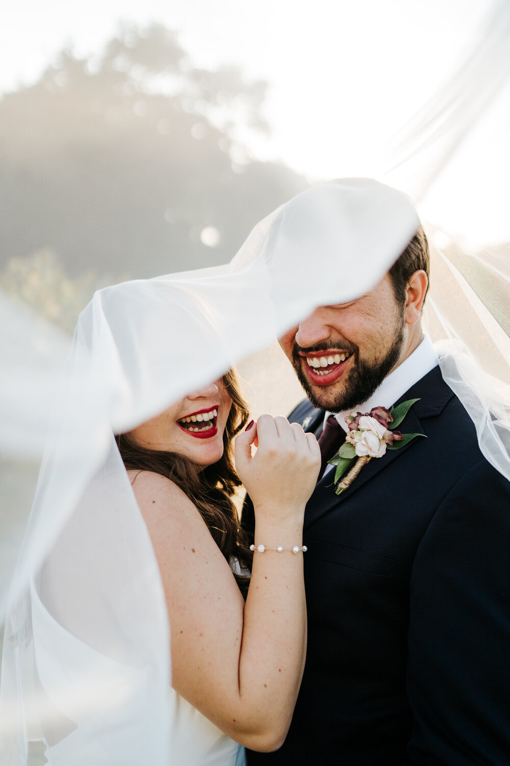 Bride and groom smile at camera as their eyes are covered by wedding veil