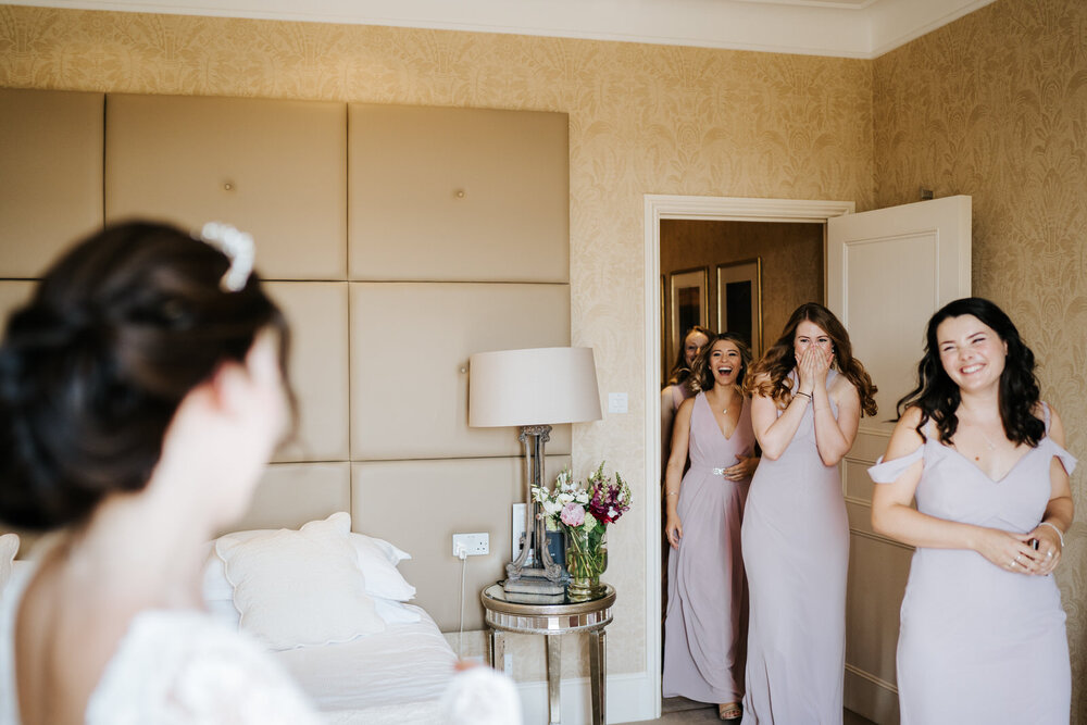 Bridesmaids see bride in her dress for the first time and are incredibly excited 