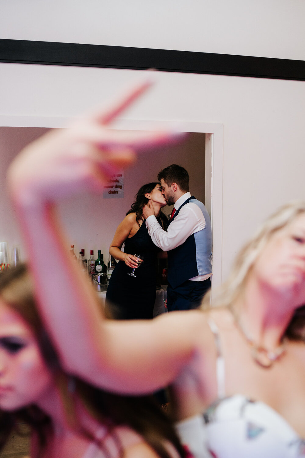 Guest motions towards camera as couple are seen kissing and embracing in the background