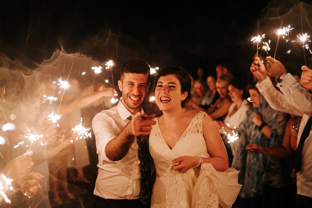 Bride and groom point at camera as they walk down a tunnel of sparklers at Pembroke Lodge wedding