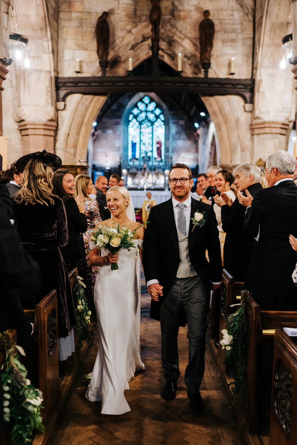Bride and groom hold hands and walk back down the aisle as husband and wife while smiling at their guests 