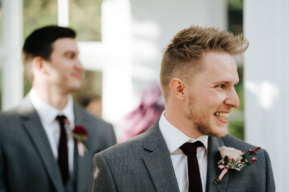 Groom is at the front of the aisle and reacts to seeing the bride walking down the aisle