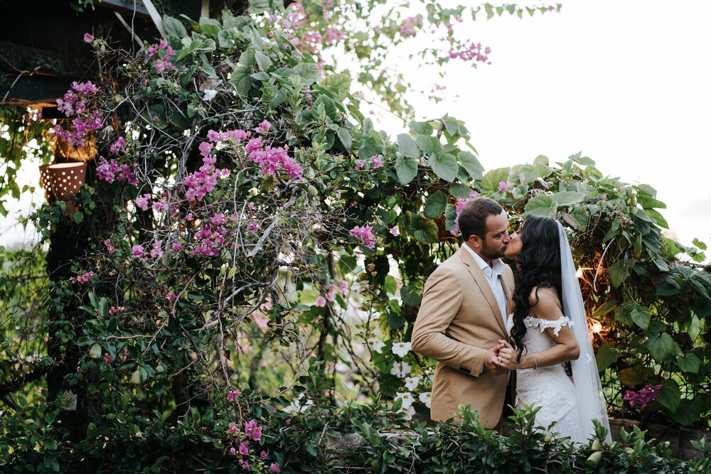 Bride and groom hold hands and kiss under beautiful pink flowers (Copy)