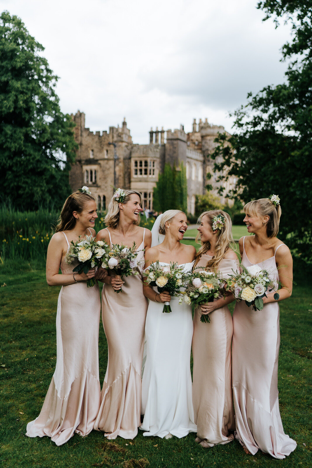  Smiling photograph of bridesmaids and bride holding bouquets with Hawarden Castle in the background 