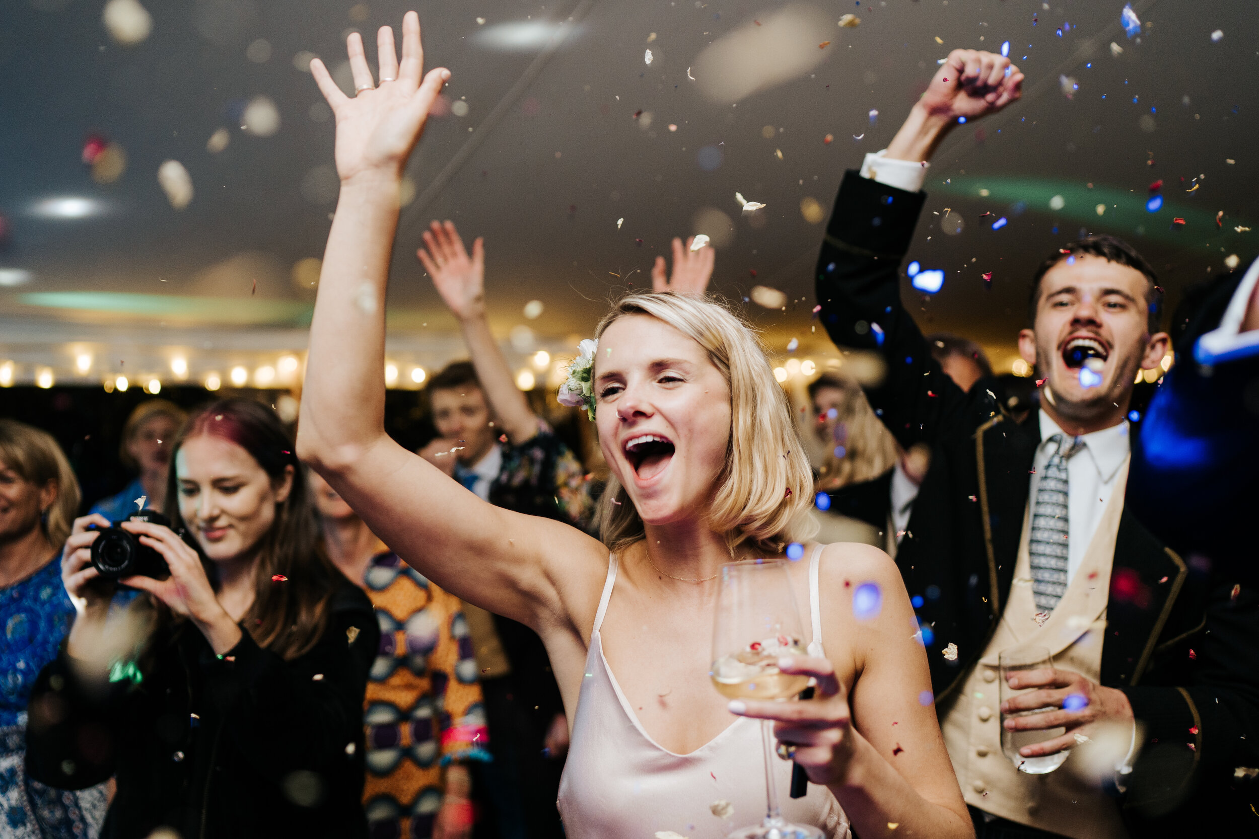 Sister of the bride and guests smiling and cheering as confetti explodes over the dancefloor