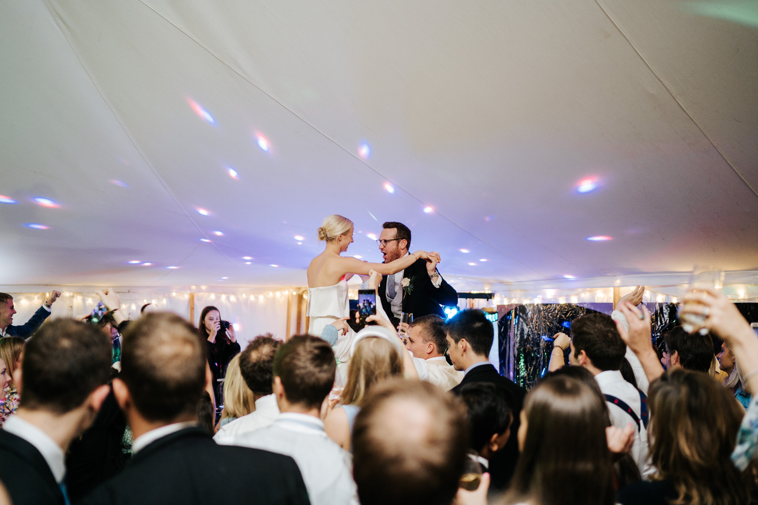 Bride and groom sit on the shoulders of guests while the dancefloor cheers them on