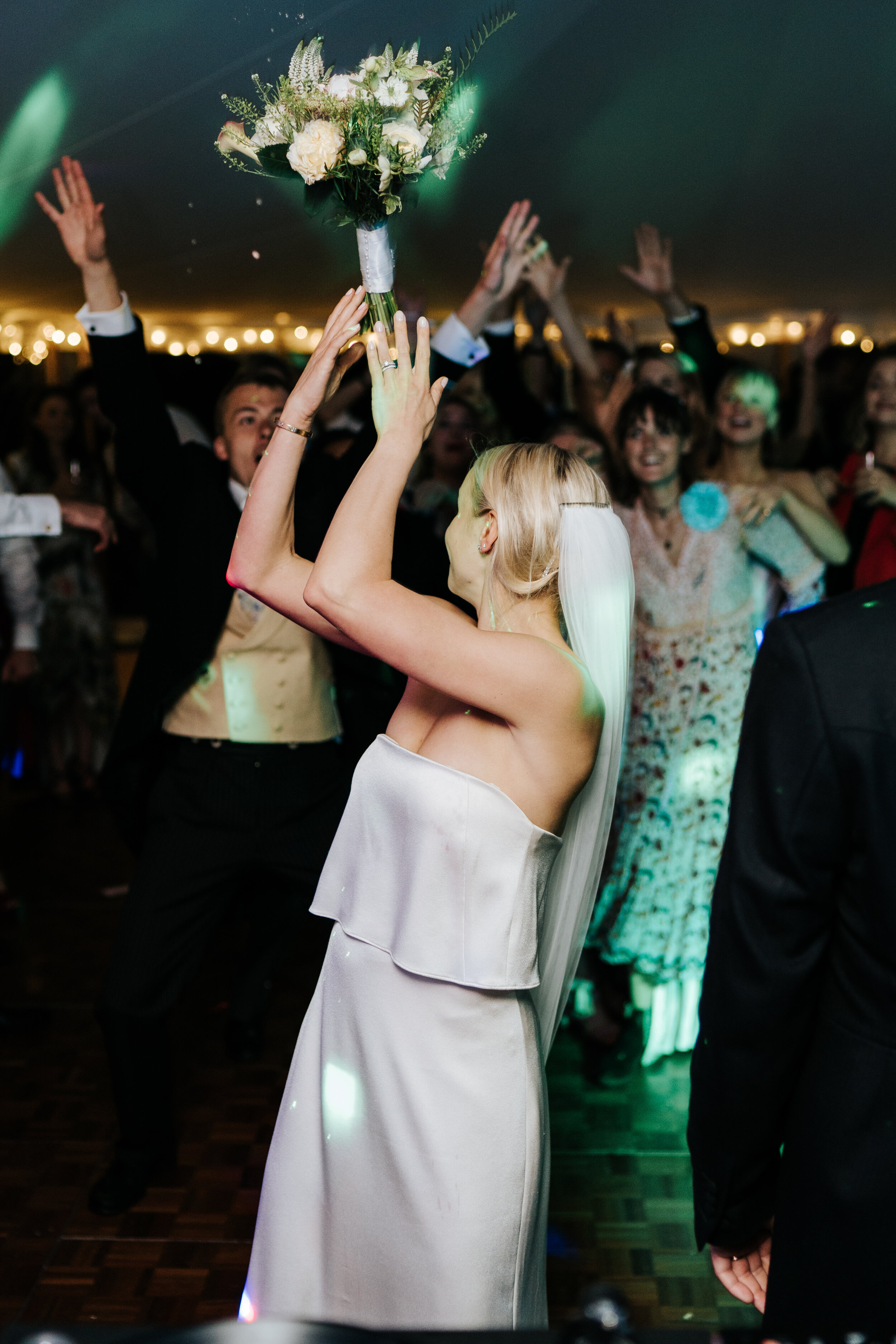 Bride throws bouquet into crowd of keen guests on the dancefloor