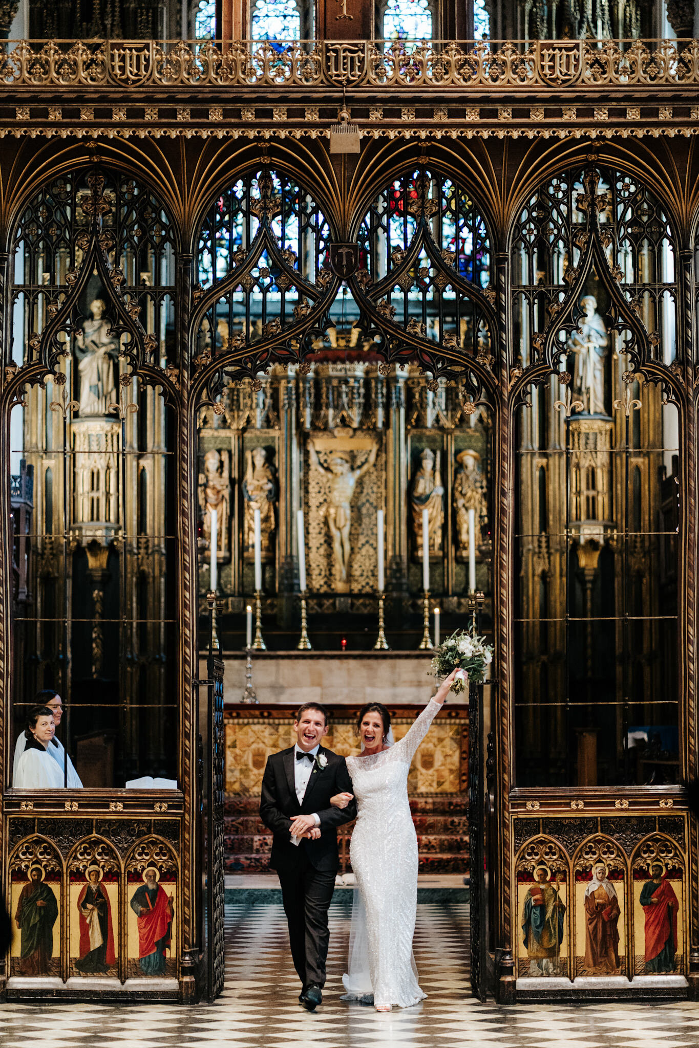 Bride and groom walk back down the aisle as a married couple at St Pauls Knightsbridge as bride throws her hands up into the air