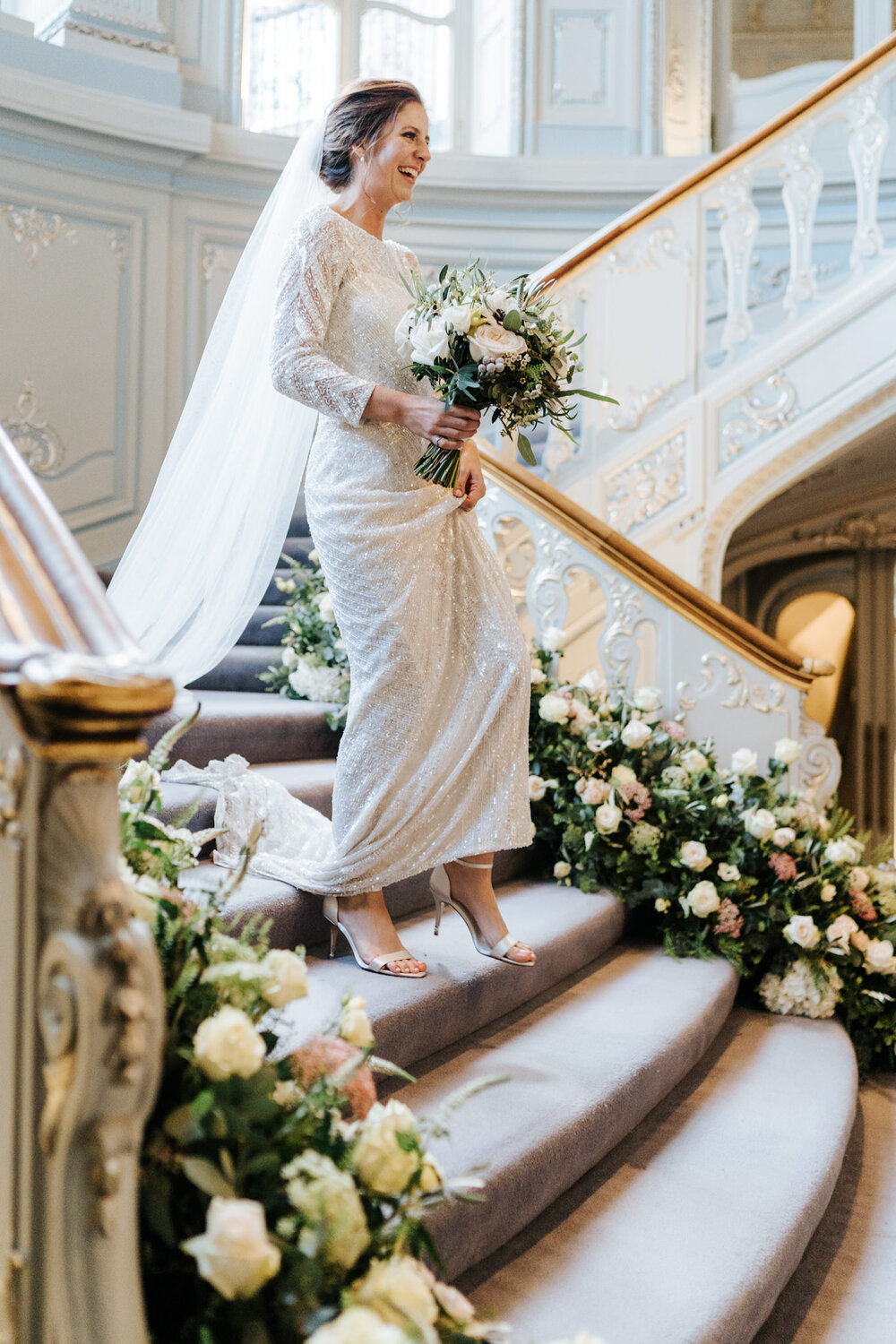 Bride walks down the flower decorated stairs at Savile Club in London before guests begin to arrive for the wedding breakfast