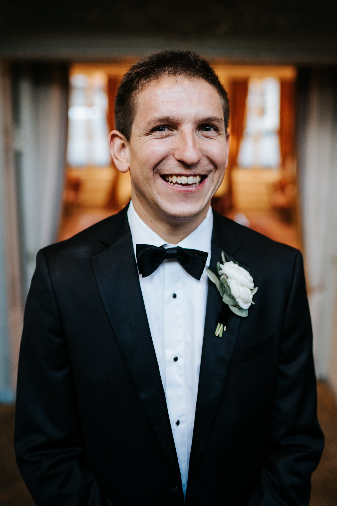 Portrait of the groom on the stairs at Savile Club London as bride, off-frame, makes him smile