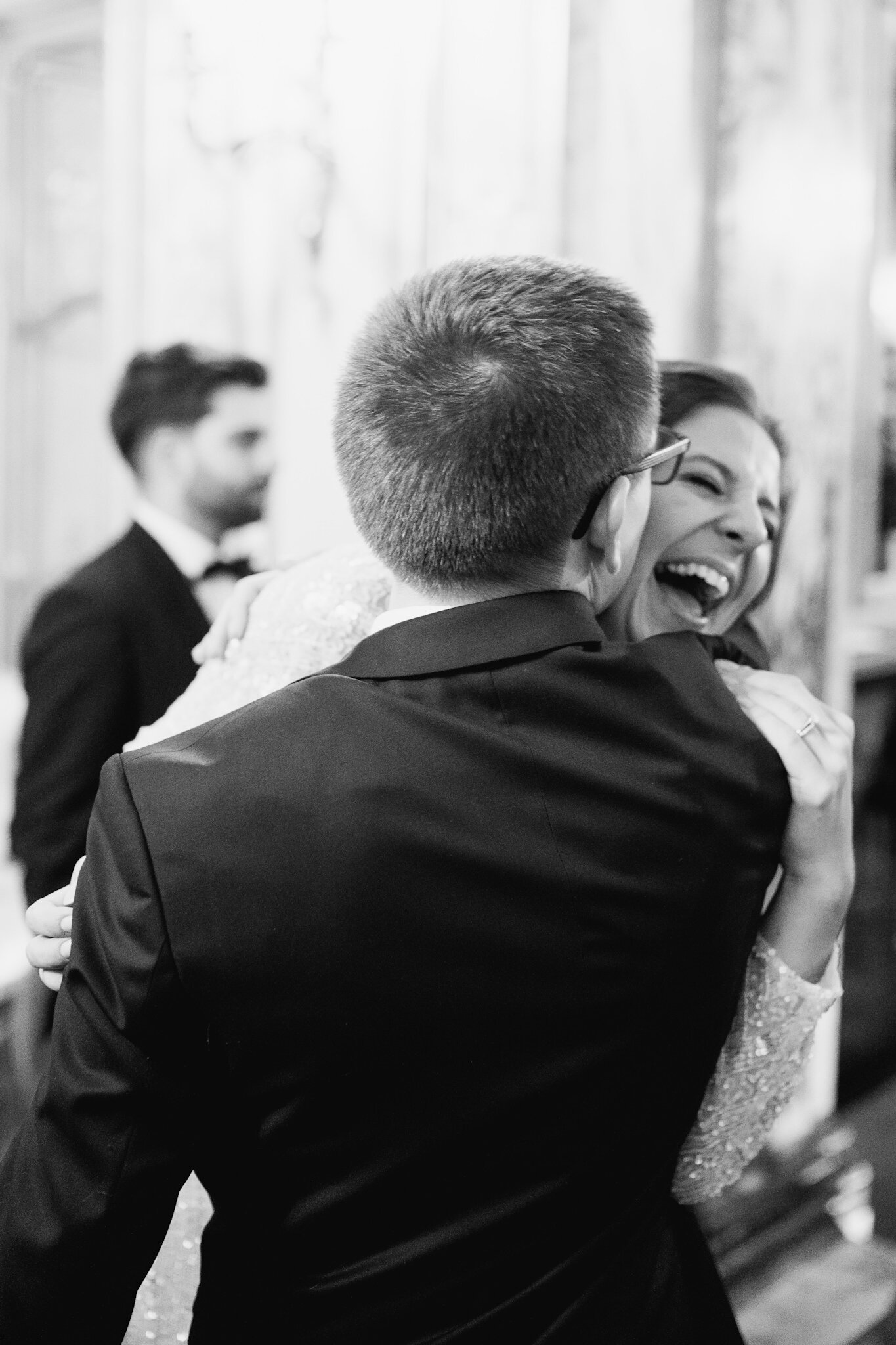 Black and white photograph of groom hugging bride as she cannot contain her laughter