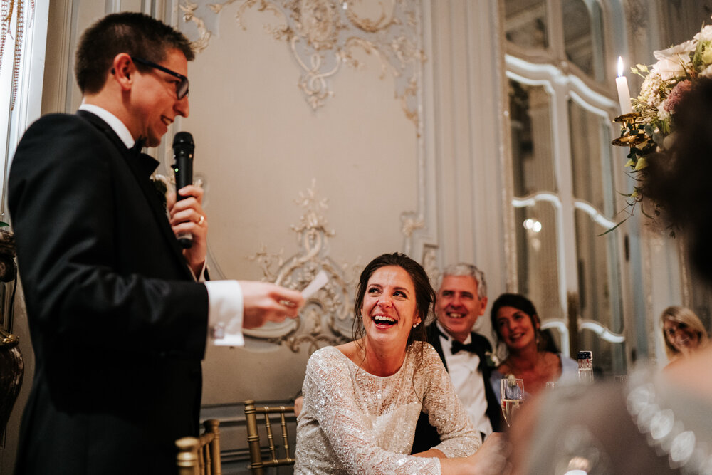 Groom delivers his wedding speech as bride and parents of the bride look at him with pride