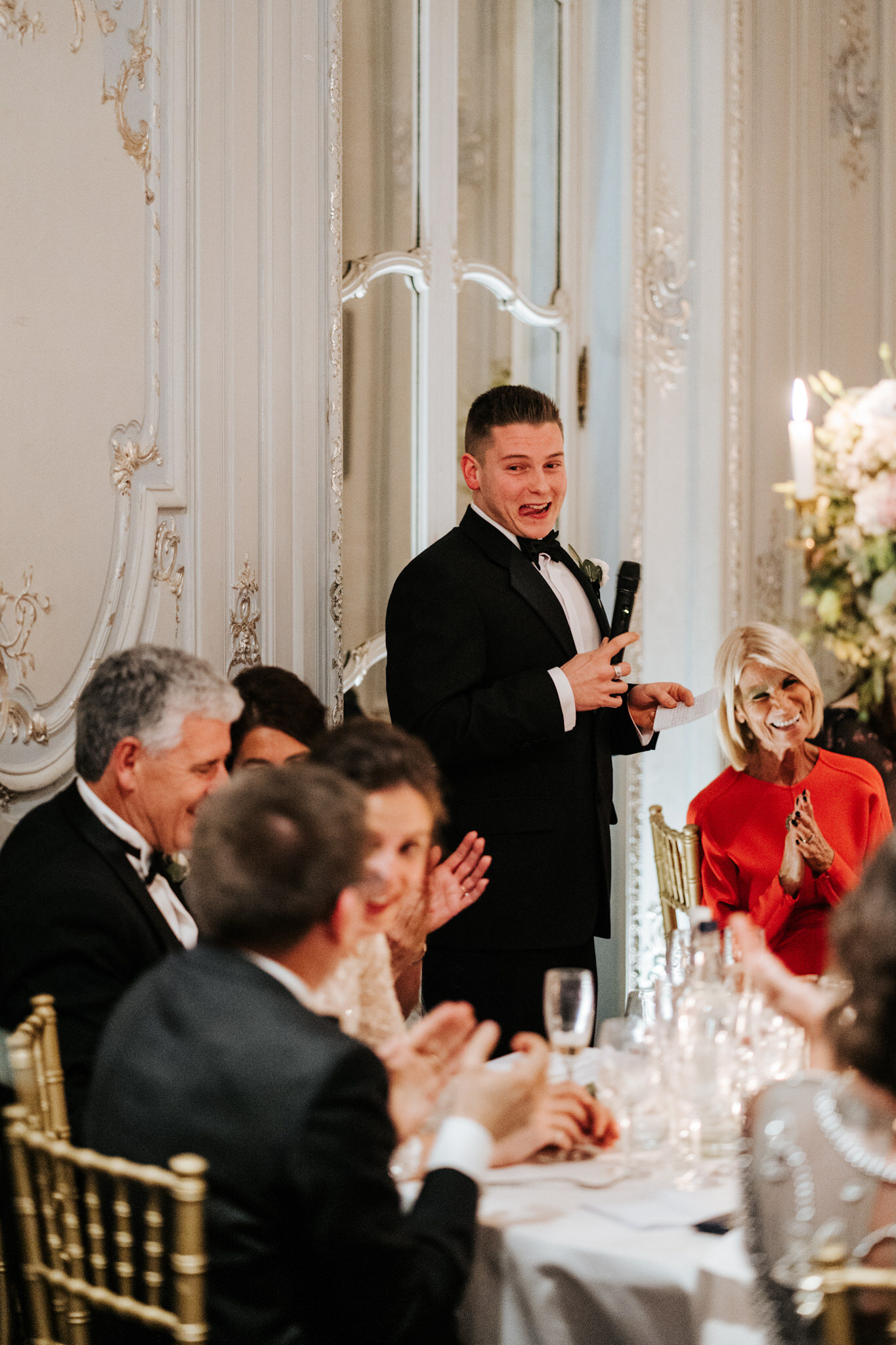 Best man holds microphone and purses lips as he gets prepared to make fun of groom during his wedding speech