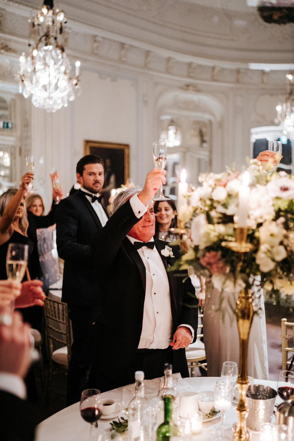 Father of the groom raises his glass as everyone around him toasts the newly married couple