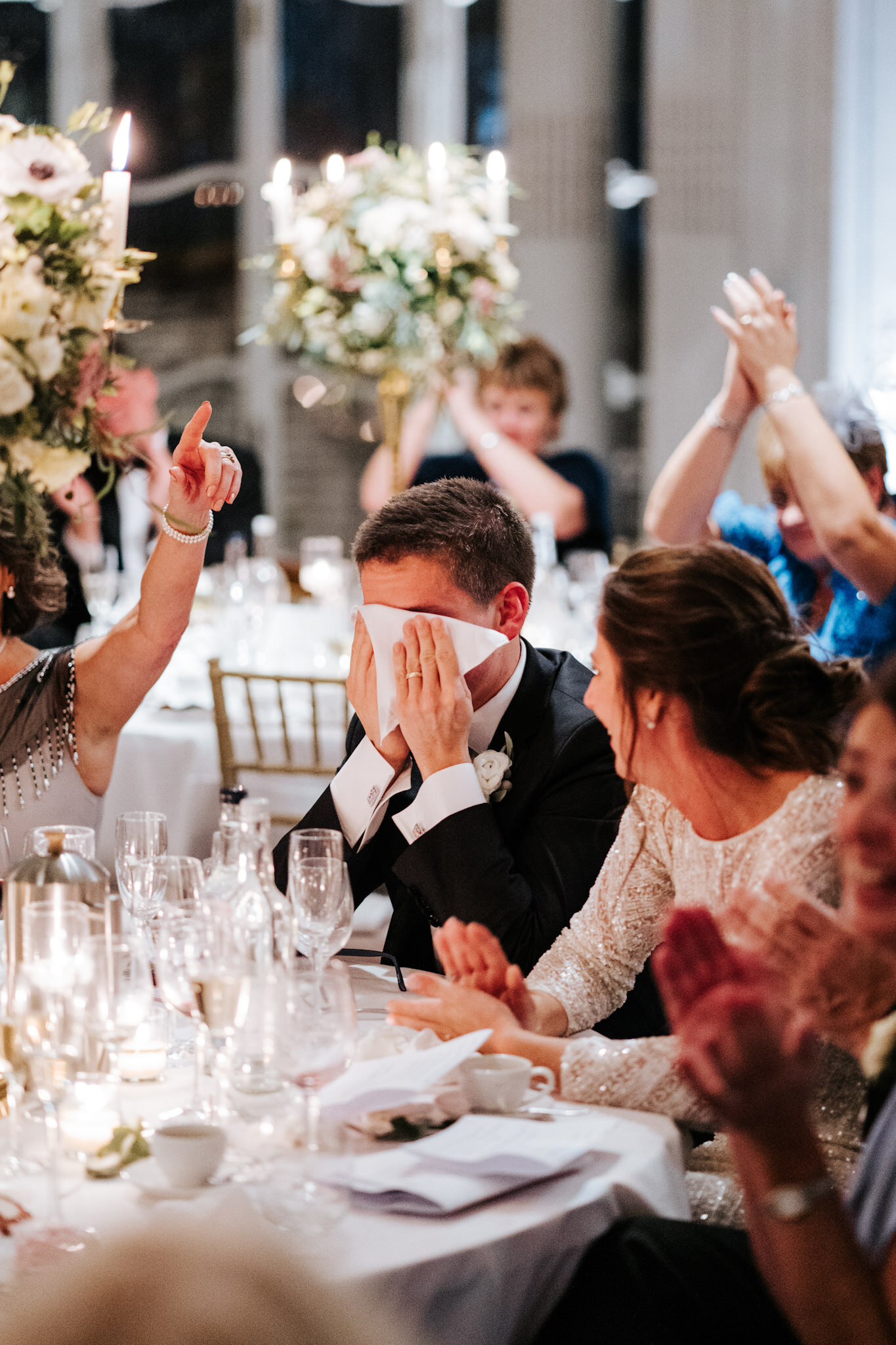 Groom wipes his tears as everyone around him claps while best man finishes his wedding speech