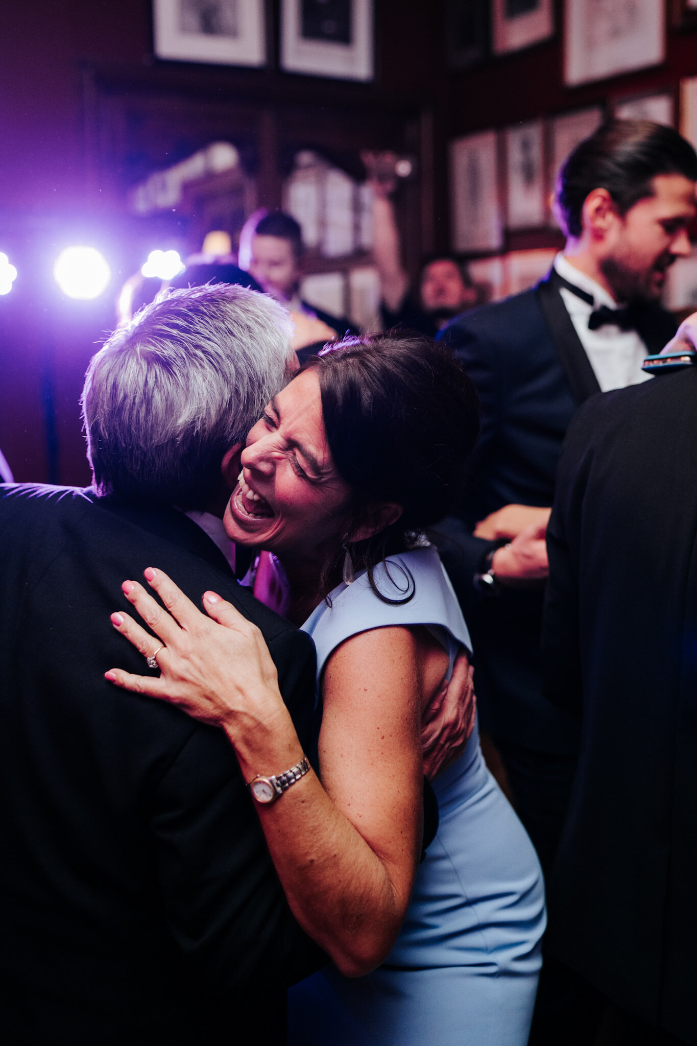 Mother of the bride and father of the bride hug as guests around them dance