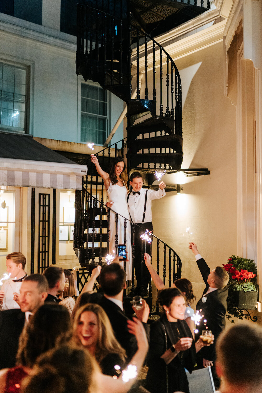Bride and groom stand on staircase at Savile Club's courtyard while waving sparklers in the air