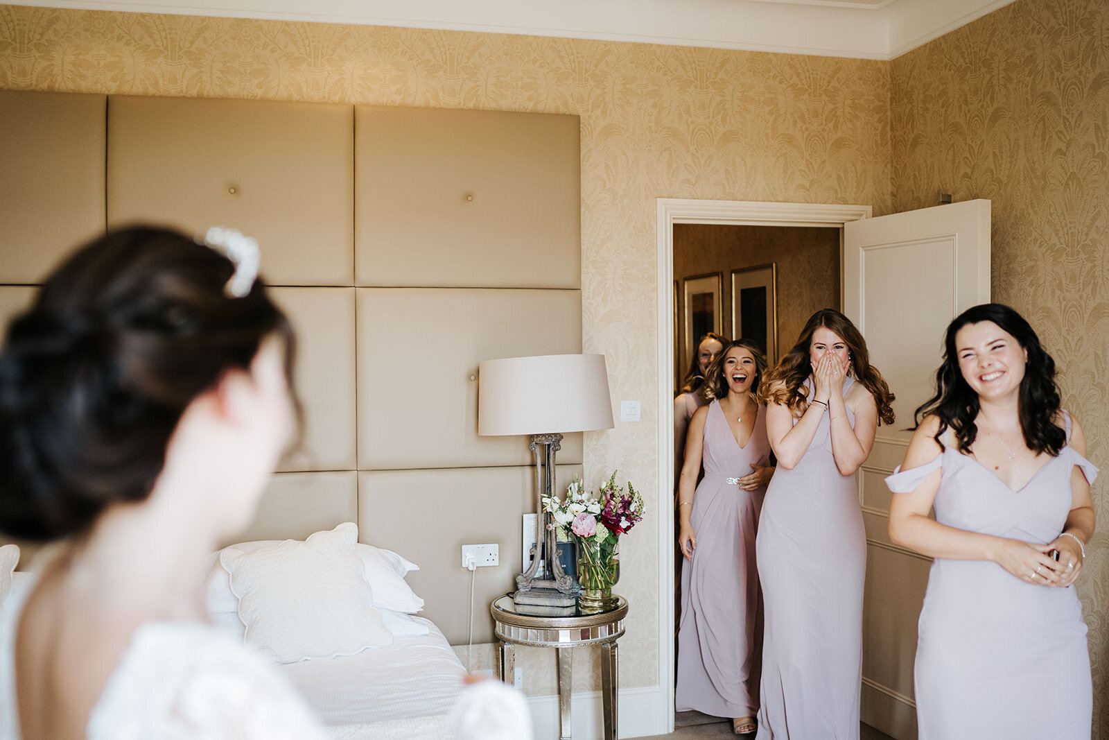 Bridesmaids enter the room full of smiles as they see the bride, standing left, in her dress for the first time for a Kew Gardens wedding