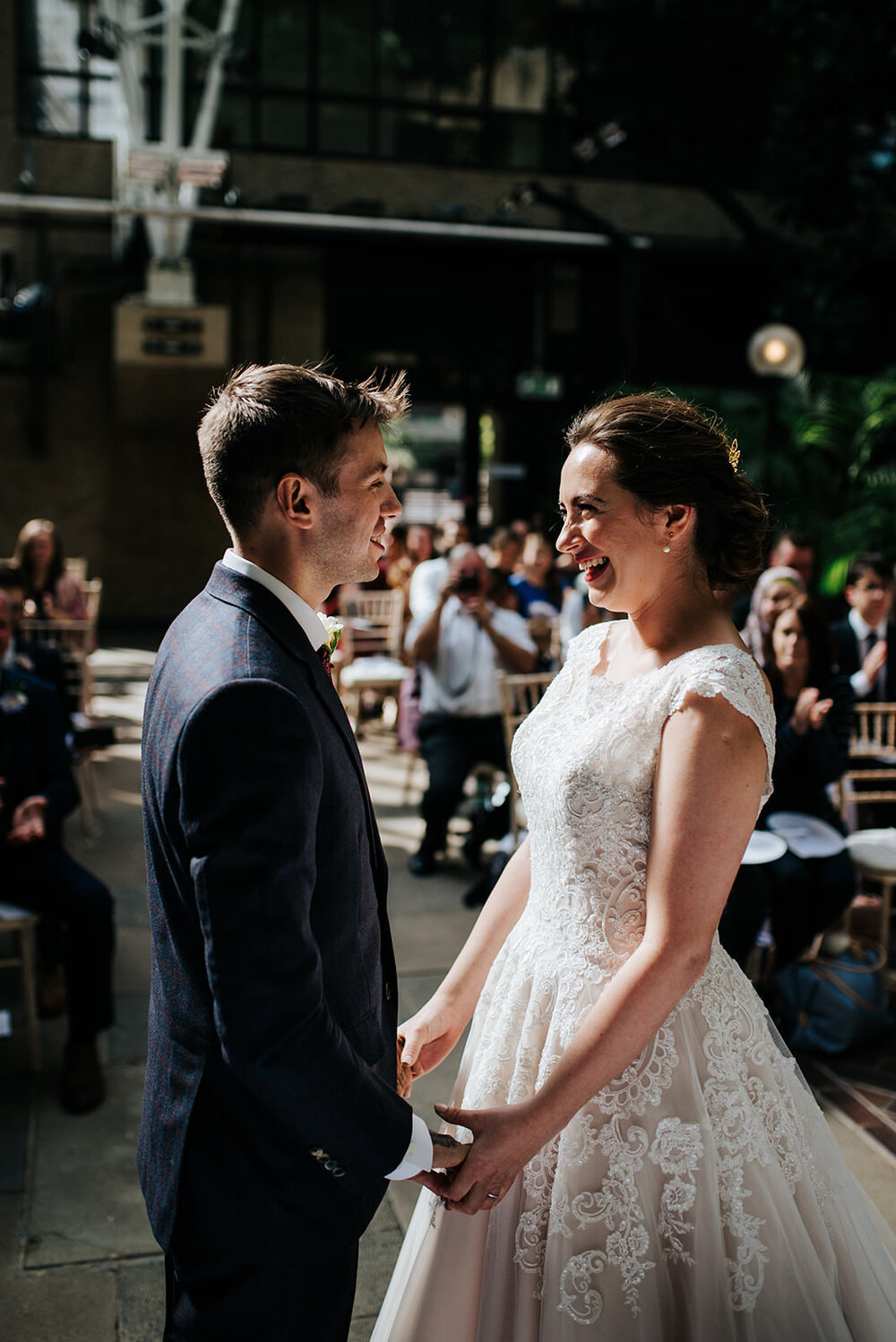 Bride and groom hold hands and look at each other passionately seconds after sharing first kiss at Barbican Centre wedding in London