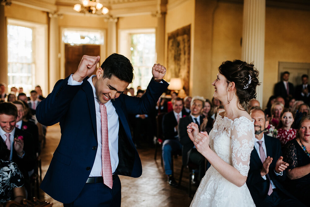 Bride and groom throw their hands up in the air seconds after their first kiss during Hampton Court House wedding in Richmond, London