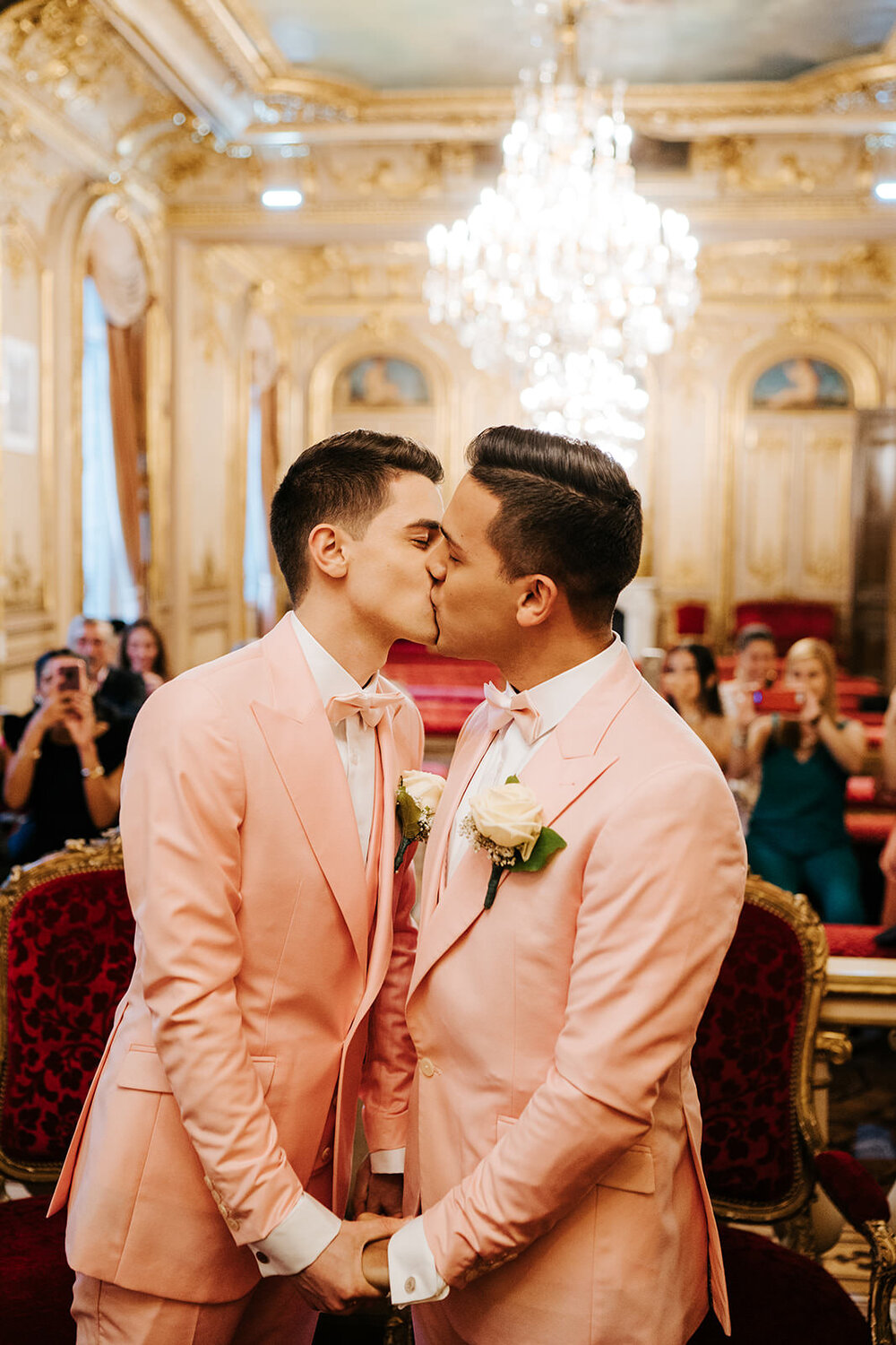 Two grooms in pink tuxedos kiss and hold hands during wedding ceremony in Paris
