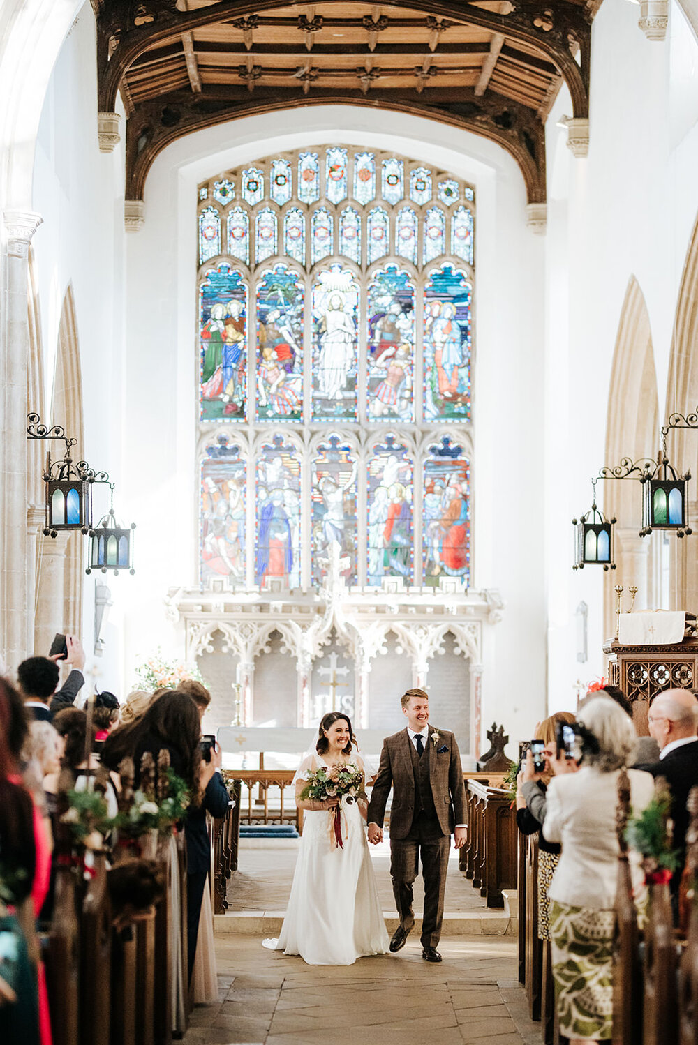 Bride and groom walk back down the aisle as married couple in opulent church with stained glass in the background