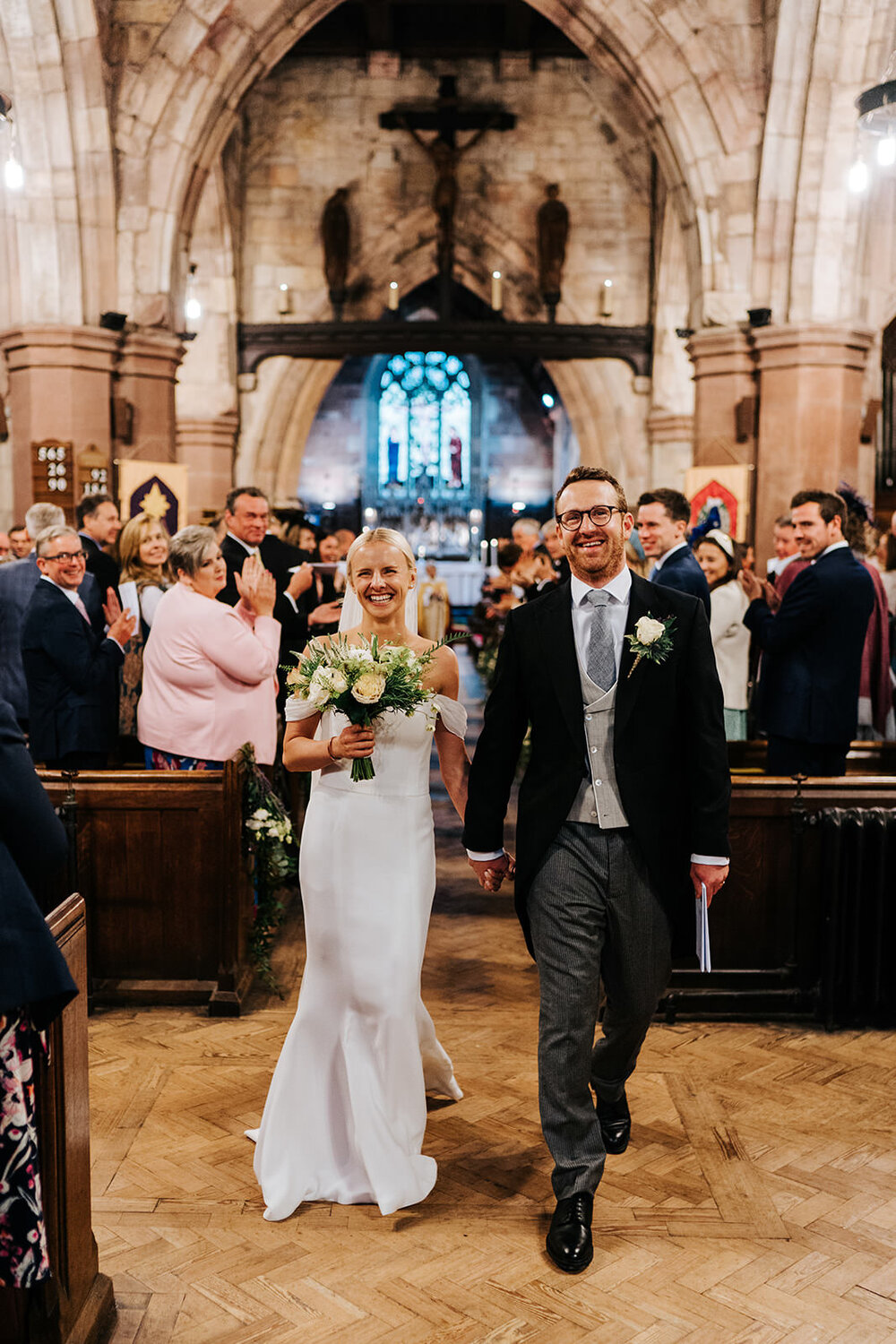 Bride and groom, smiling ear to ear, walk back down the aisle in church in Hawarden, Wales 