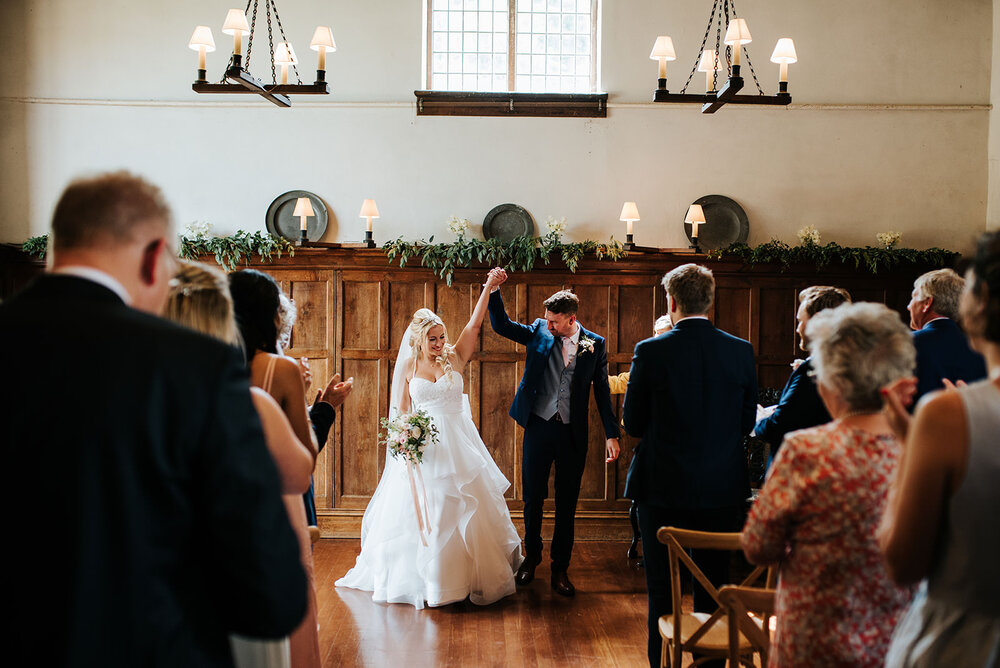 Bride and groom hold hands and elevate them into the air in celebration as wedding ceremony ends