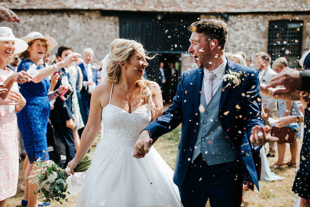 Bride and groom look at each other in pure elation as they walk out of their ceremony and are thrown confetti by their guests