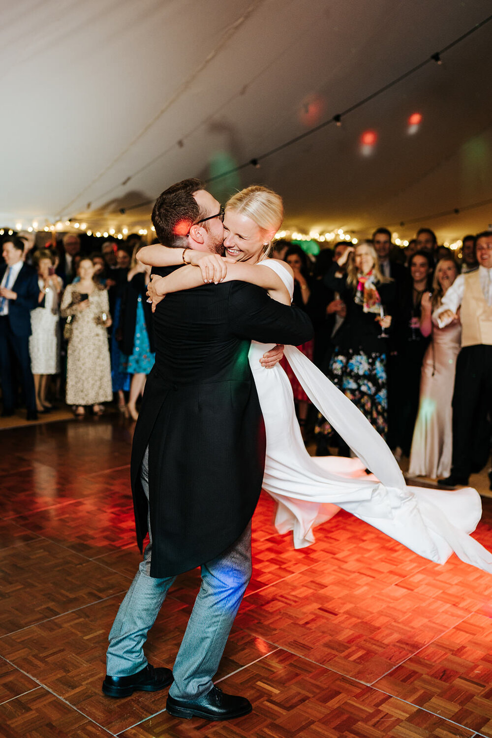 Groom lifts bride up and twirls her around during first dance in Hawarden, Wales while DJ lights go off in the background