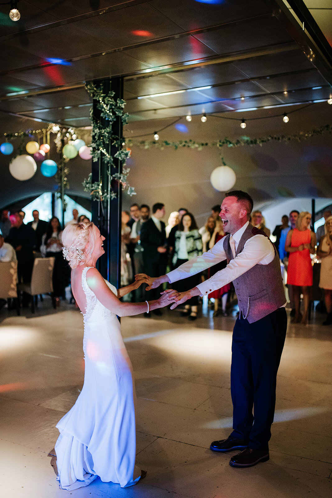 Bride and groom hold hands at arms' length and smile at each other during first dance in English countryside wedding