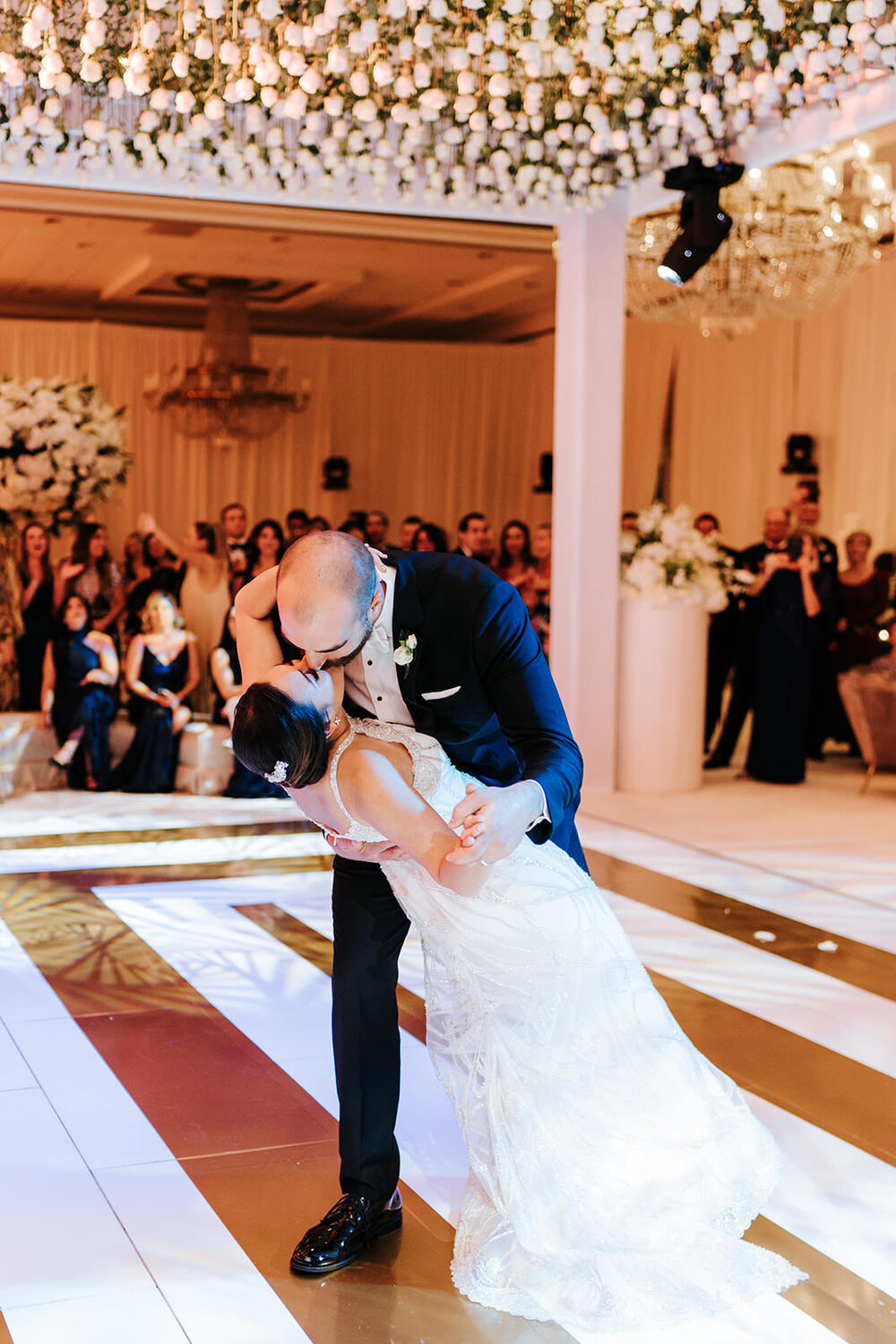 Groom dips and kisses bride during first dance at luxurious hotel in Puerto Rico under a dancefloor ceiling of white roses