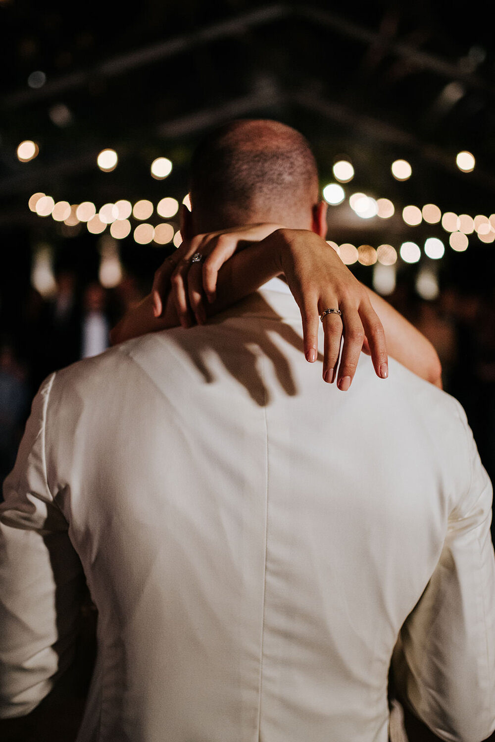 Photograph of the back of the groom with bride's hands resting elegantly slightly over his shoulders during first dance at wedding in Puerto Rico