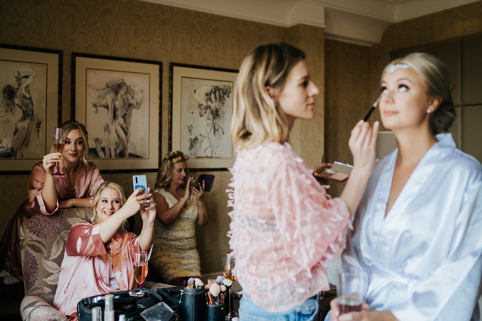 Bride has her make-up done in foreground as bridesmaids take selfies in background at The Petersham Hotel 