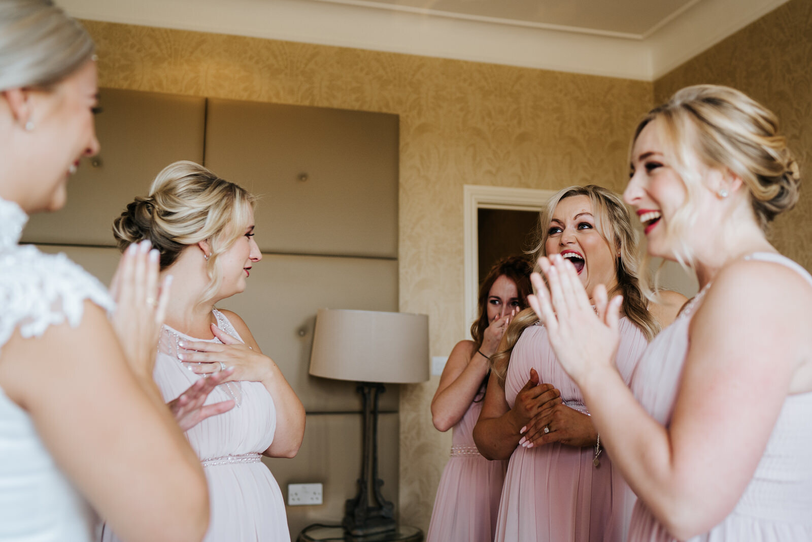 Bride and bridesmaids gather around each other and smile as they are excited for the wedding day ahead