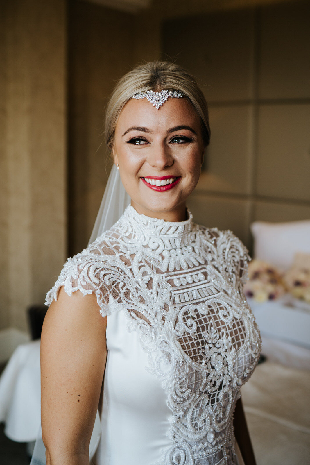 Bride smiles and has tears in her eyes as she stands and looks out the window in portrait during wedding prep at The Petersham