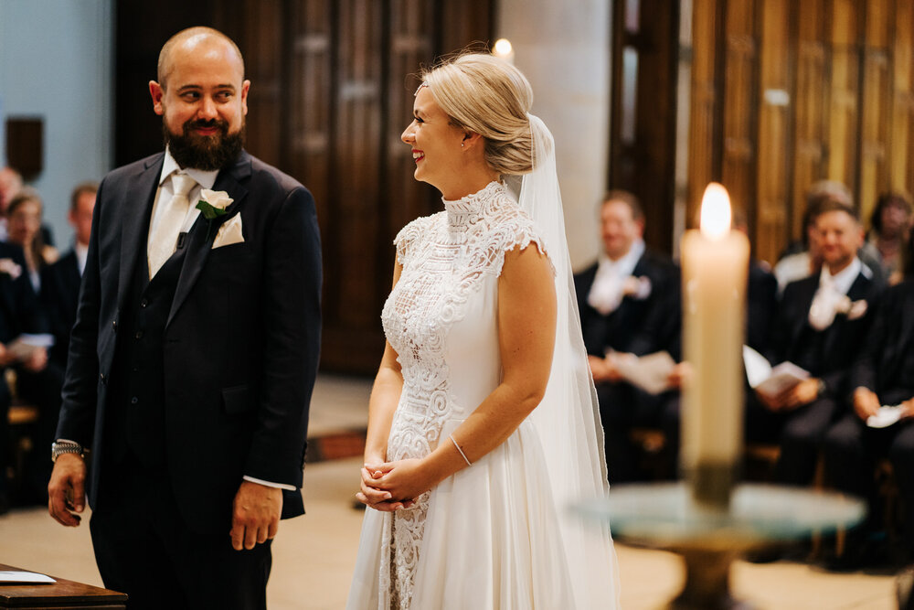 Bride and groom look at each other and smile as they stand at the front of the aisle in St Matthias Church in Richmond