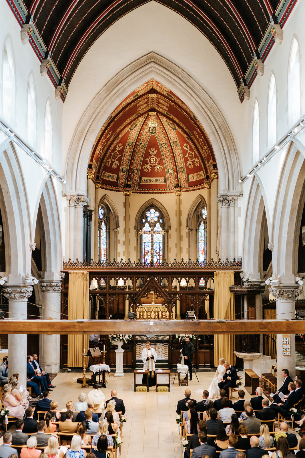 Wide photograph taken from the back of the church showing all of the guests and the couple during the wedding service at St Matthias Church in Richmond