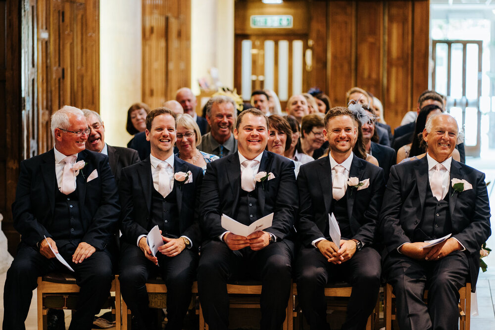 Ushers and groom's dad sit and laugh in first pew as the service is underway at St Matthias Church in Richmond 