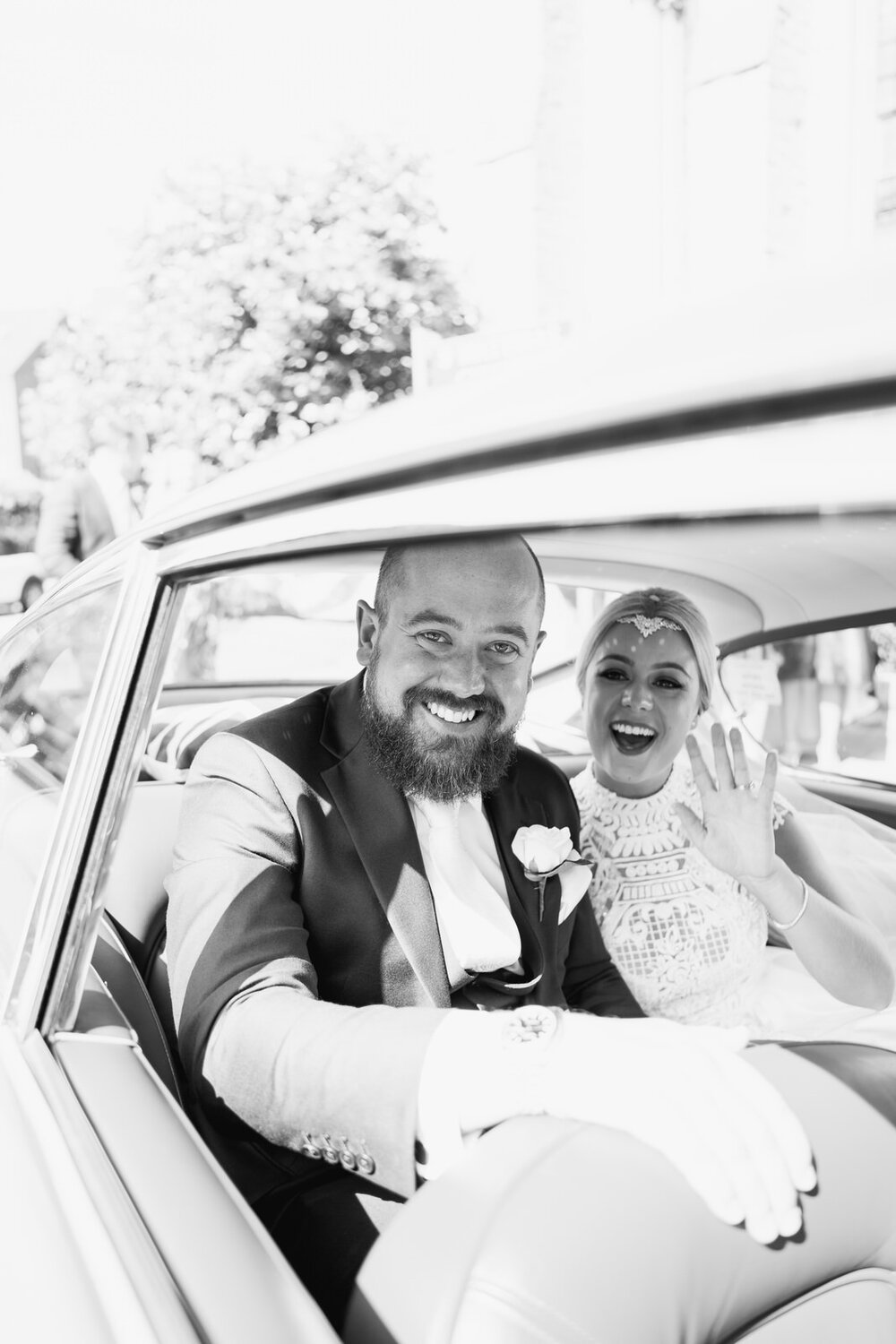 Black and white photo of the couple in their vintage car, smiling and laughing, seconds before departing for wedding at Pembroke Lodge in Richmond Park