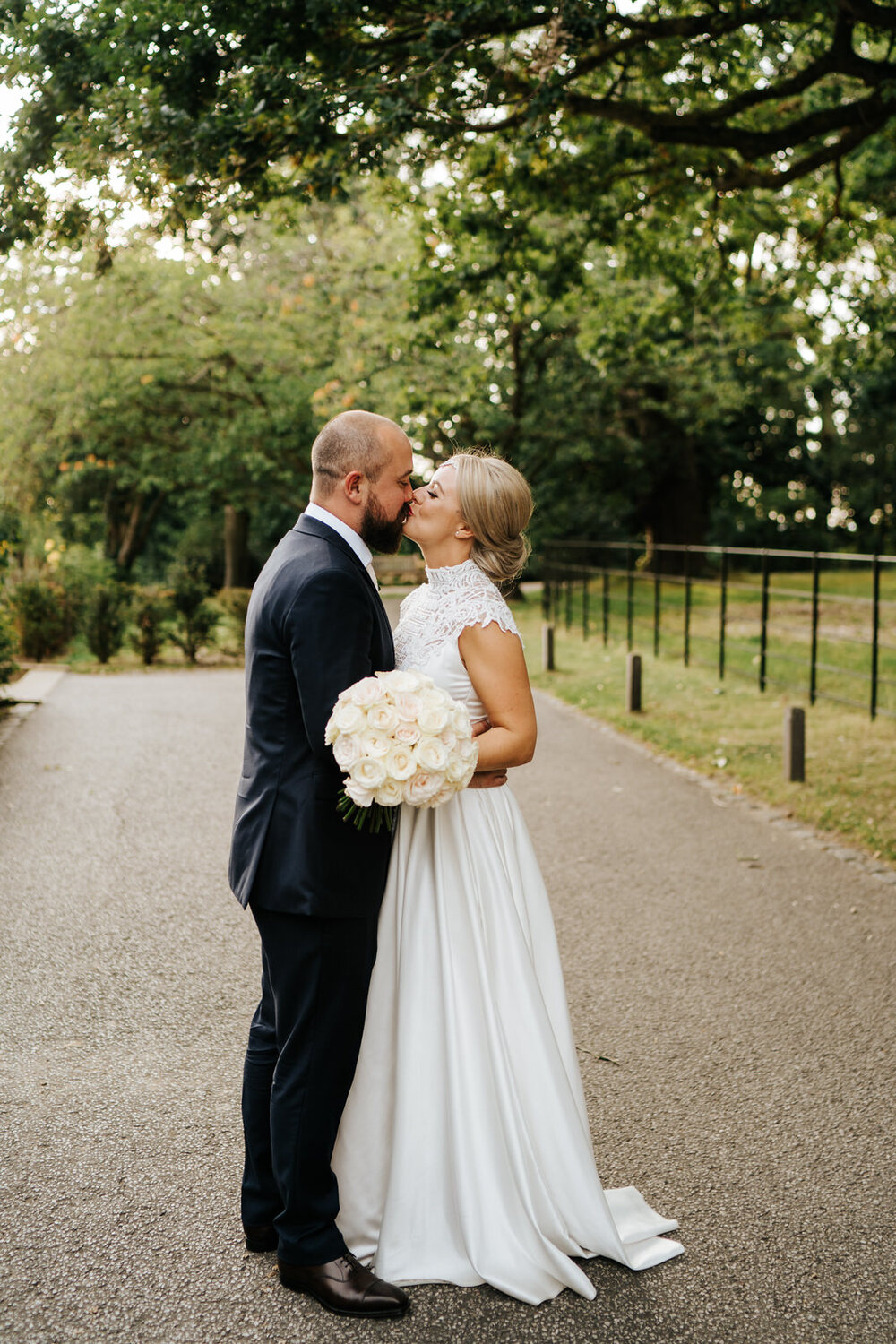 Bride and groom stand close to each other and kiss as they walk around the grounds of Pembroke Lodge for wedding photographs