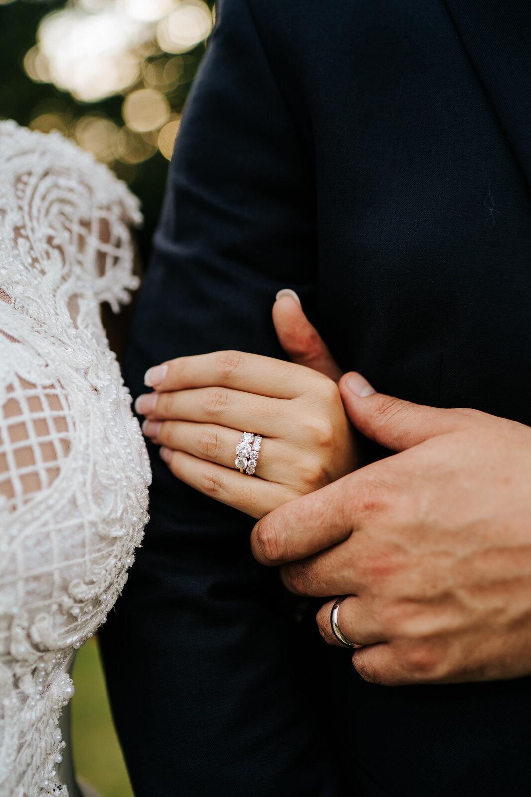Close-up photograph of the bride and groom's hands with additional focus on the diamond ring