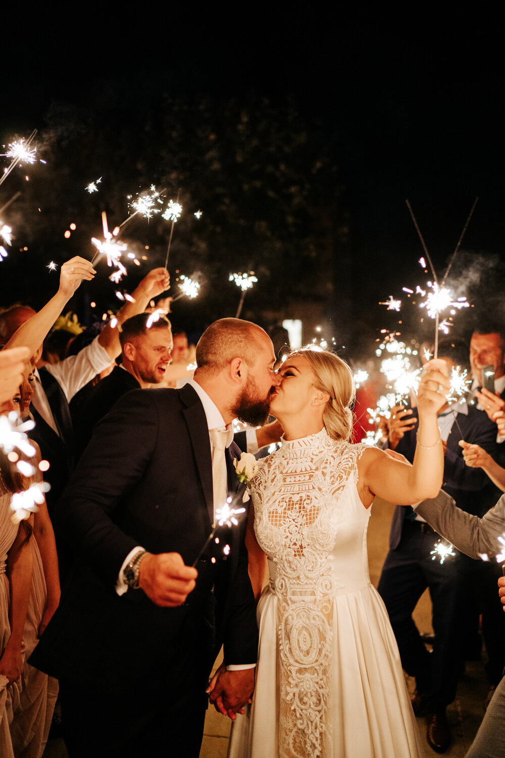 Guests form a tunnel of sparklers around the bride and groom as they hold sparklers and kiss in gorgeous framing outside at Pembroke Lodge during nighttime