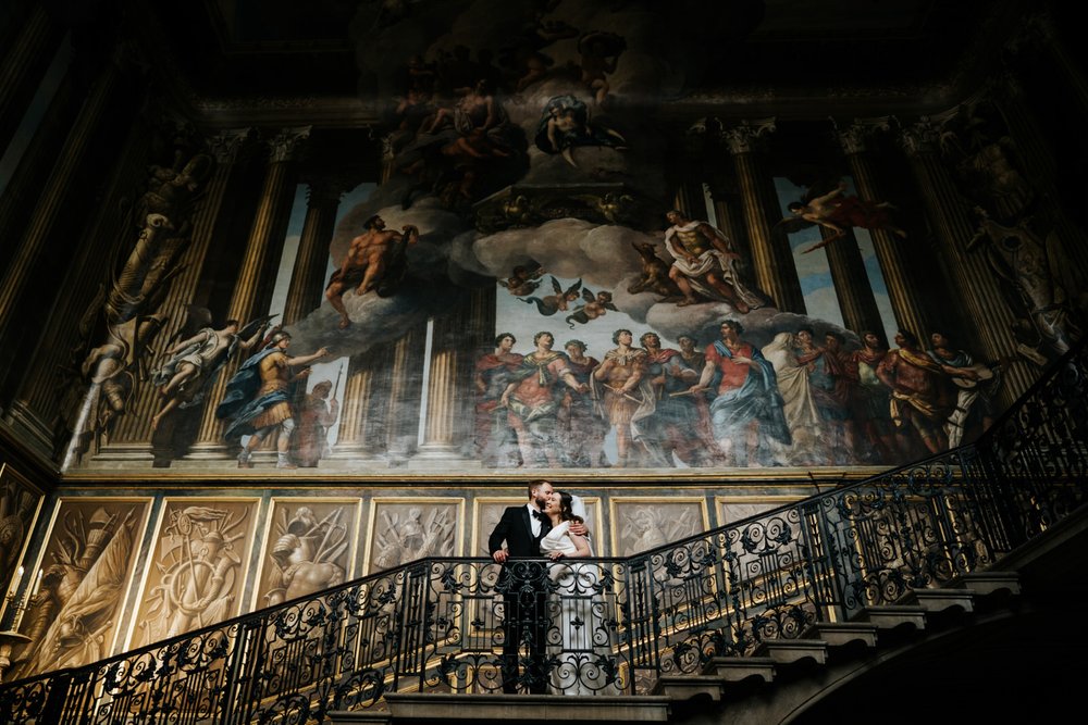 Bride and groom pose in front of majestic painting at Hampton Court Palace in gorgeous wedding portrait