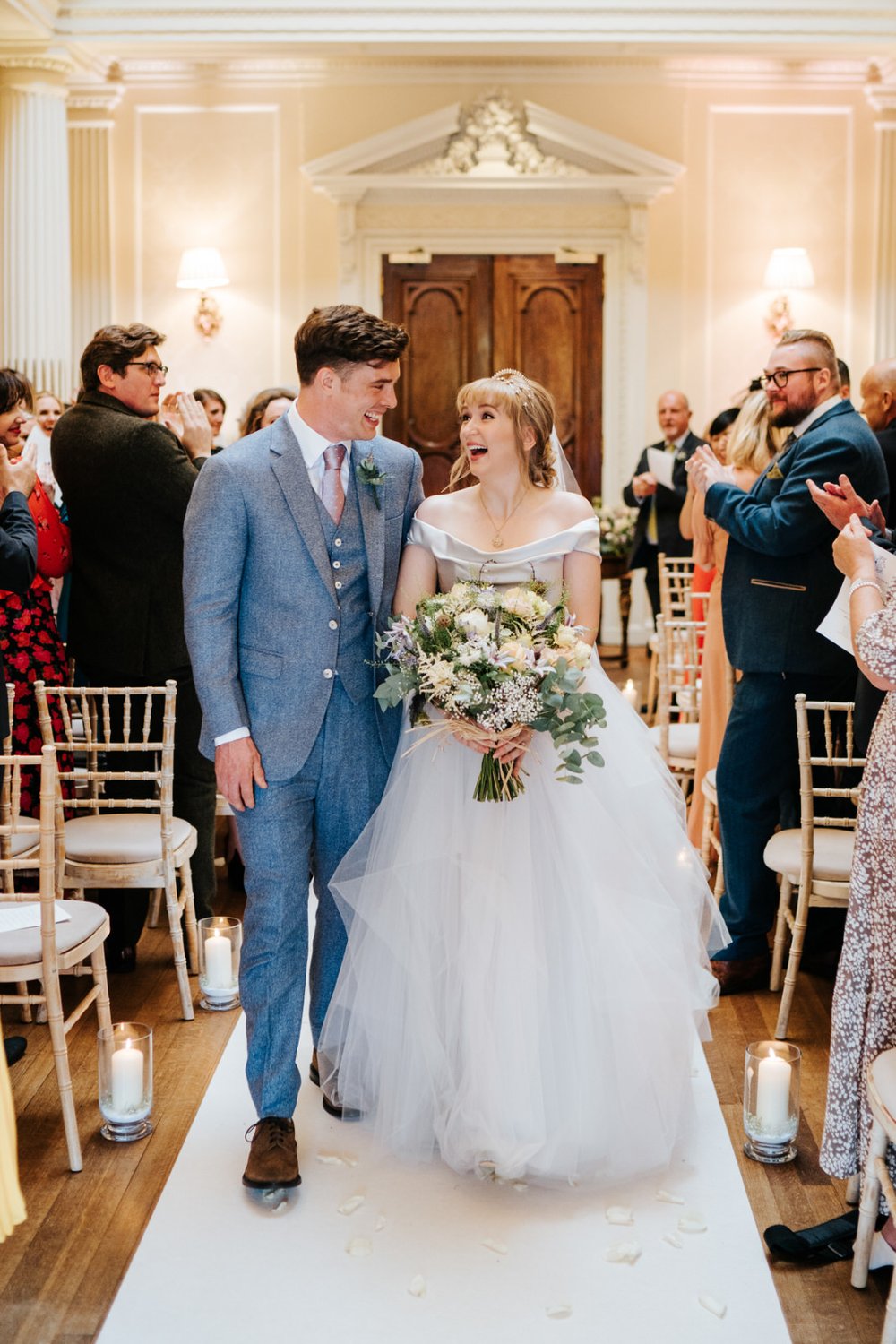 Bride and groom walk down the aisle right after their ceremony and cannot contain their excitement as they look at each other and smile at Hedsor House Wedding