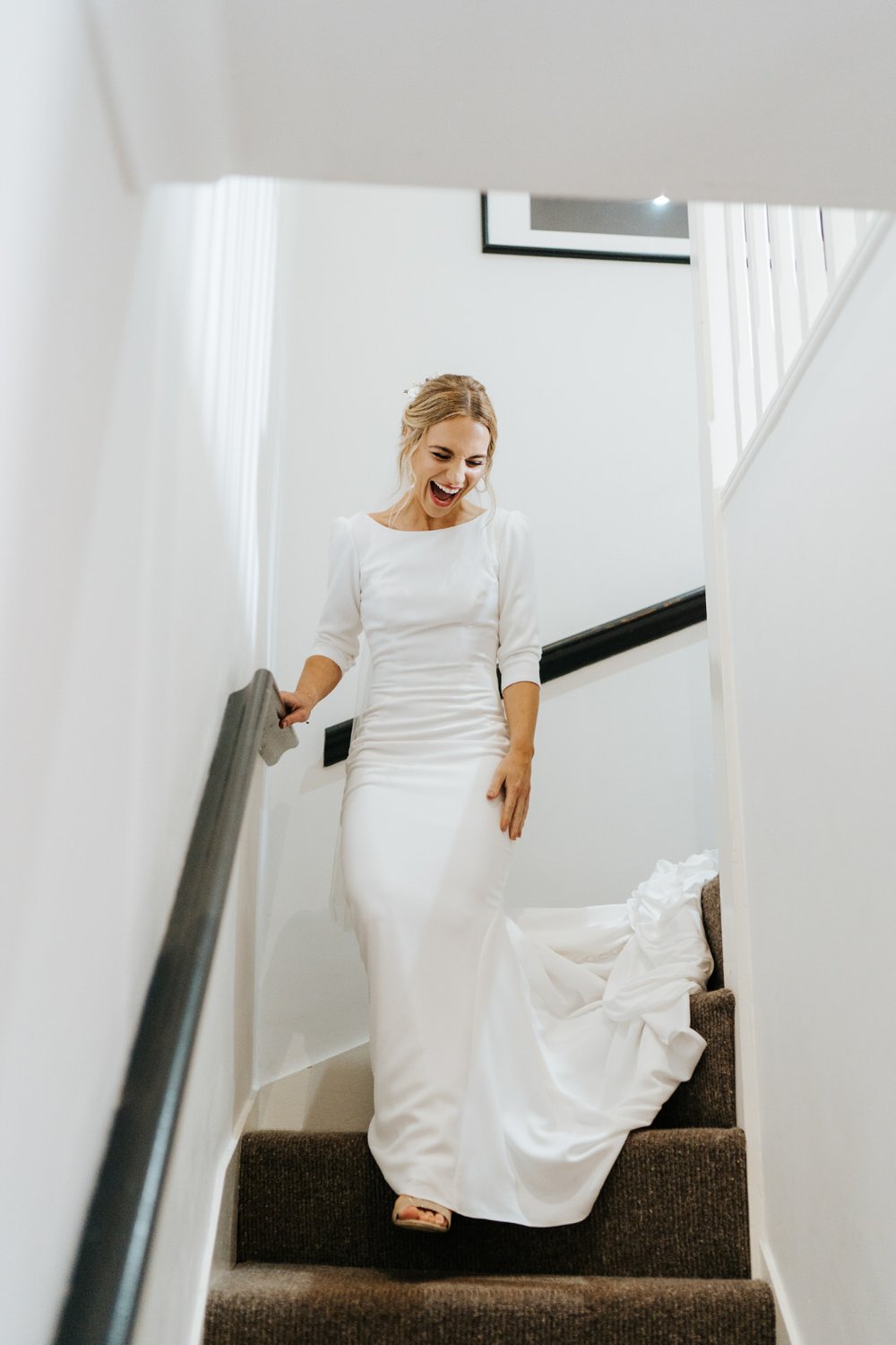 Bride walks down the stairs at her house wearing her dress and full of excitement for everyone to see her wearing it